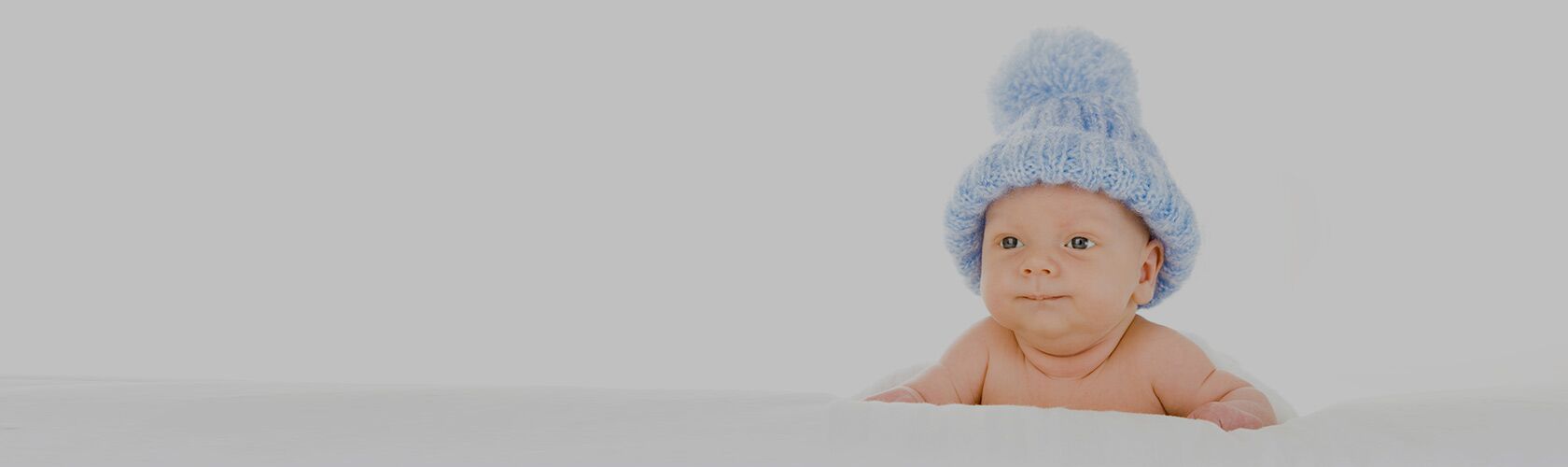 Ein Baby mit blauer Wollmütze liegt auf dem Bauch und schaut neugierig in die Kamera.