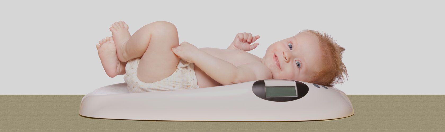 Ein Baby liegt lächelnd auf einer Babywaage, während es gewogen wird, passend für den Verleihservice.